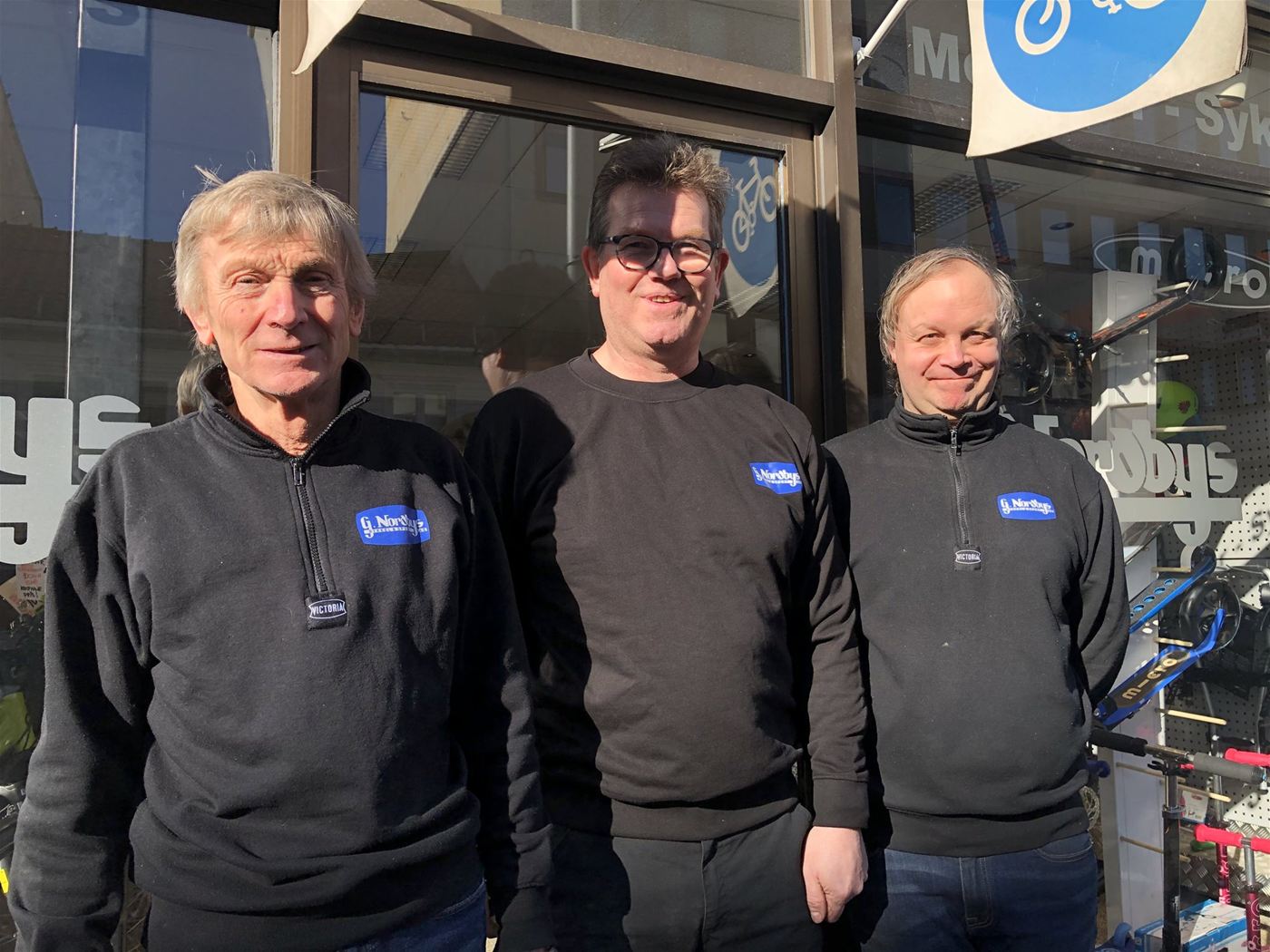 Tre ansatte i G. Nordby-gensere foran butikkvinduet